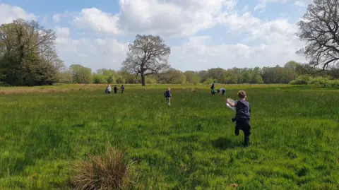 Julia Moore / BBC A group of children with their backs to the camera. They are in an open field with trees in the background.