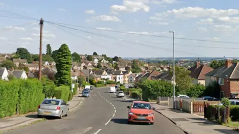 A streetview image of Cavendish Road. It is a single carriageway residential street with trees and shrubbery on either side. Cars can be seen parked along the road