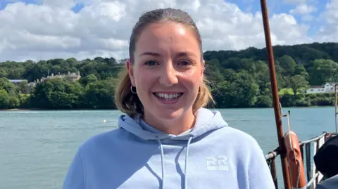 Anna Hume smiling at the camera, standing in front of the water of the Menai Strait