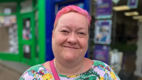 A woman with pink hair, smiling in the street