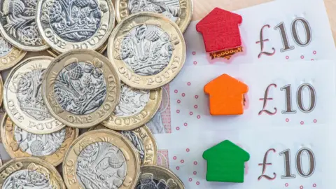 Getty Images Pile of notes and coins and small wooden representations of houses.