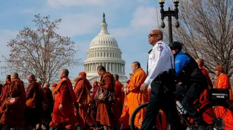 A crowd of monks wearing orange from head-to-toe walk past the Capitol building in Washington DC.