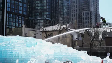Toronto Fire crews spray water on a large ice block installation created to promote rapper Drake's upcoming album.