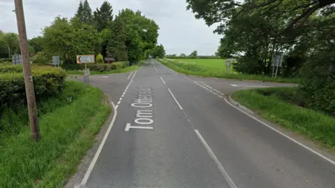 A Google Street View screen capture of the junction the crash took place near. It is a rural B road with fields and trees surrounding. 