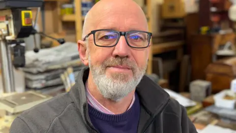 A head and shoulders photograph of East Lindsey District Council leader Craig Leyland. He has a beard and is wearing glasses, and he is smiling at the camera.