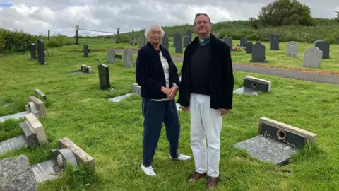 Churchwarden Carole Roberts and Reverend Chris Painter standing amongst the laid-down gravestones