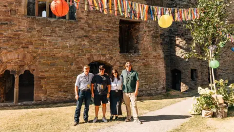 Hanglands Four people stand in a castle courtyard decorated with colourful bunting and hanging lanterns.