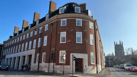 An old fire station that has been transformed into housing. The building is red brick and has white rectangular windows.