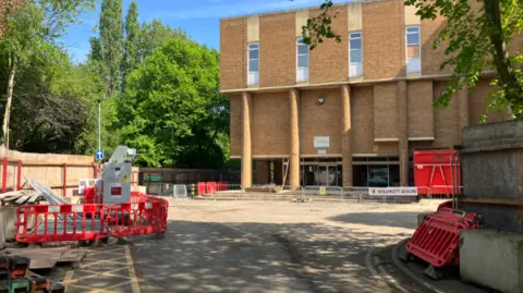 Shariqua Ahmed/BBC Exterior building of the regional pool with metal grills at the entrance and construction material on site