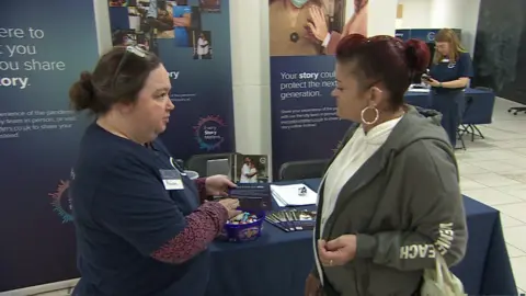 Two women talking in front of posters which are promoting the inquiry 