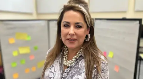 BBC Siobhan Connor wearing a patterned blouse in front of a noticeboard with post it notes