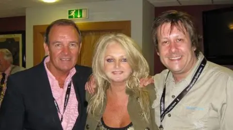 Rob Marshall A glamorous blonde woman with two men on either side of her. They are all smiling and looking at the camera.