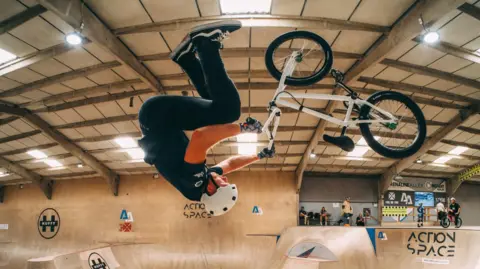 Adrenaline Alley A BMX rider performing a stunt at the skatepark. He is upside down on the ramp.