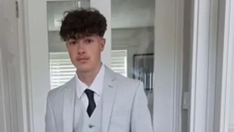 Family photo A young man with dark curly hair in a room with white walls in a white suit with a black tie