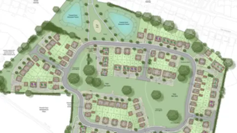 Illustrative site plan of a residential housing development showing roads, housing plots, green open spaces, mature trees, landscaped areas, and two pond features in the northern section of the site. The layout includes cul-de-sacs, a central parkland area, pedestrian paths, and an access roundabout at the southern entrance, with surrounding existing streets and properties shown in the background.