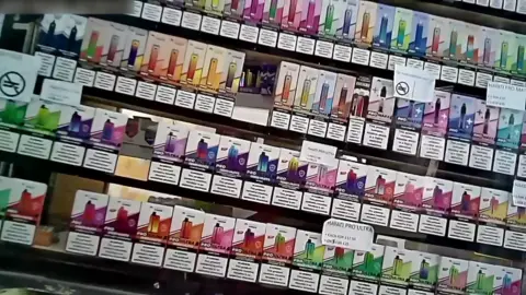 A selection of colourful vapes shelves behind a shop counter.