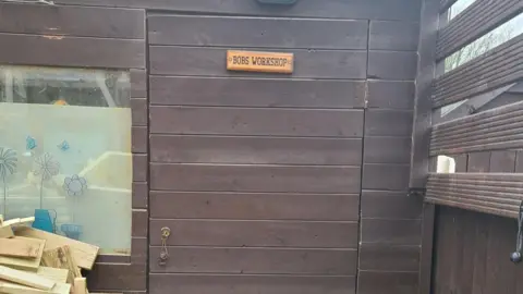 Bob Williams A brown timber door of a shed, with a sign on it saying Bob's Workshop