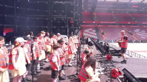 Anfield Road Primary School A group of schoolchildren on stage at a stadium.
