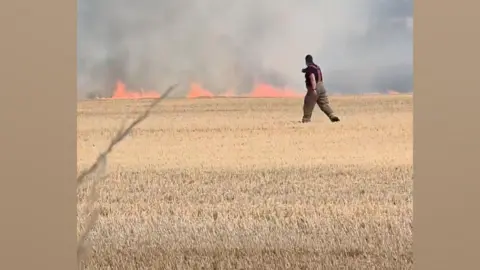 Kev Sparky A fire man walking across a field with fire in the background 