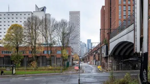 LDRS A CGI of proposals for a new development at Charles Street in Manchester showing a tower block set behind a low-rise building fronted by trees, with a bridge running to one side. 