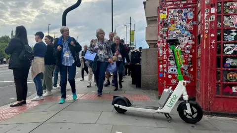 Sarah Gayton An e-scooter in the middle of the pavement on a busy street in London. 