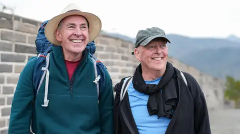 Brian Mole (left) and Melvyn Mole (right) at the Great Wall of China. They are wearing their hiking equipment including rucksacks.