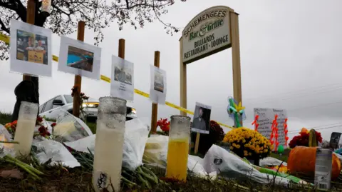 Candles, pumpkins and flowers make up a memorial next to a sign for the bar that was the site of a mass shooting