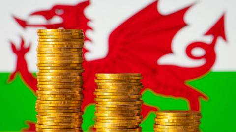 Stacks of golden coins forming going down graph on the background of flag of Wales