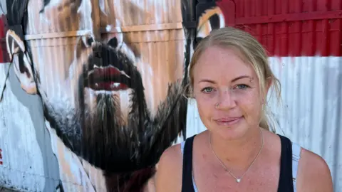John Devine/BBC Jade, a woman wearing a black sleeveless top, standing in front of the Kane mural.