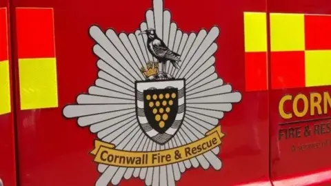 A fire service logo with a black bird and Cornwall Fire & Rescue on the side of a fiure engine.