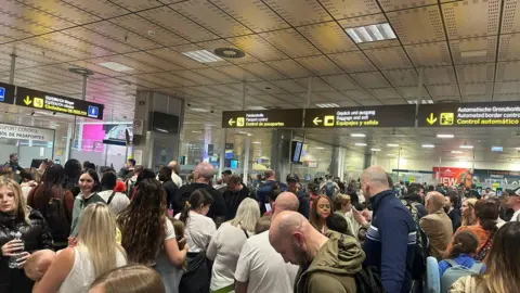 A large queue of lots of families at an airport. There are signs overhead reading "passport control" and "EU citizens"