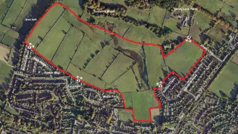 LDRS A birdseye view of the planning site, which shows green fields. There are homes to the south of the site.