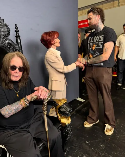 Mason Newman Mason Newman is shaking Sharon Osbourne's hand while Ozzy Osbourne sits in a chair leaning on a walking stick. Mason has brown trousers and a black T-shirt on. Sharon is in a beige outfit and Ozzy is wearing a black top and trouser and shades.