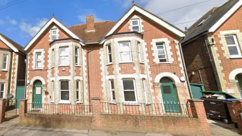 A pair of red brick semi-detached houses with green front doors. 