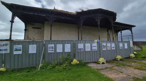 A dilapidated bandstand building, with fences set up around it.