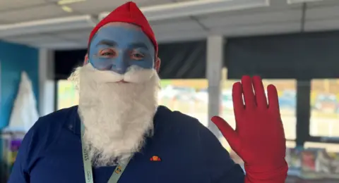 A man dressed up as a Smurf with a blue face, a beard, and a red hat and gloves.