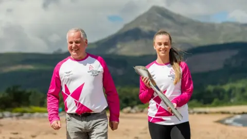 Getty Images Former Scottish First Minister Jack McConnell, now Lord McConnell, hands the baton to badminton player Eleanor O'Donnell on Brodick beach