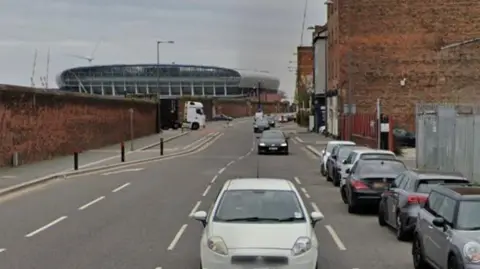 A road showing a merge of two lanes into one as a cycling lane starts. A steam of cars can be seen on one side of the road.