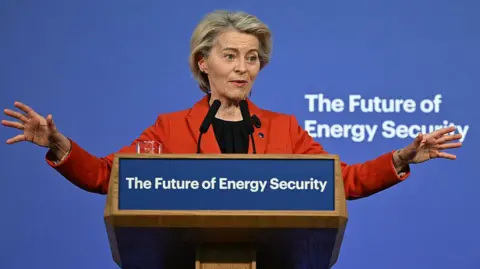 AFP A woman in an orange jacket speaks at a lectern