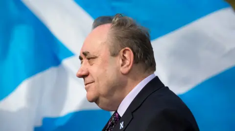 PA Media Alex Salmond is side-on to the camera with a Saltire emblem  down  him