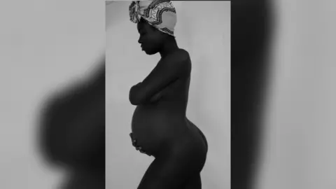 Krissima Poba Nagouma / Eye Mama Project Krissima Poba Nagouma pictured side on in silhouette, with her baby bump showing as she cradles it with her hand. She is wearing a head scarf which contrasts with the black silhouette of her, as it is white.