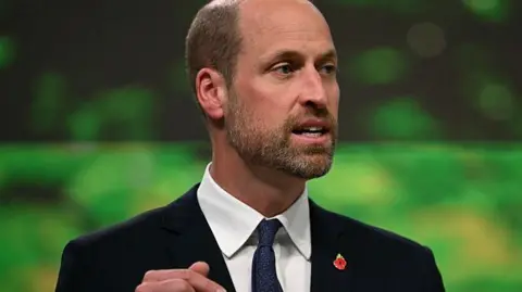 Getty Prince William in a dark suit, white shirt and dark tie. He has a red poppy pin on his lapel. 