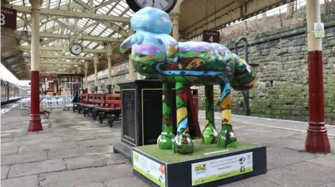 Bury BID A colourful sheep sculpture is positioned on a platform in the middle of a railway station. This sculpture is a homage to all the UK’s farming lands, featuring different aspects throughout the seasons within one image.