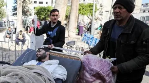 Two men wheel an injured man on a bed with a drip