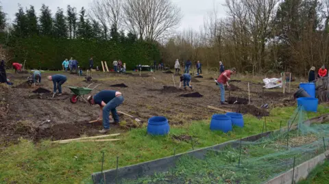 Peter Thompson People digging in brown soil in an outdoor space