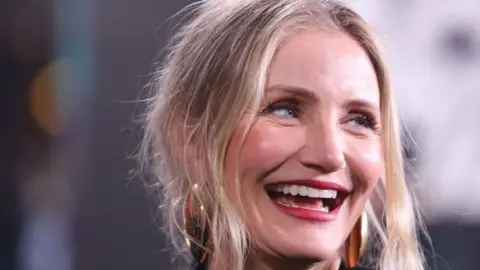 Cameron Diaz smiles to her left in a close-up portrait photograph taken on a red carpet.