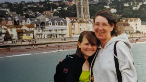 Ezzy Pearson An old photograph, potentially from the nineties, of a teenage girl and her mum smiling at the seaside