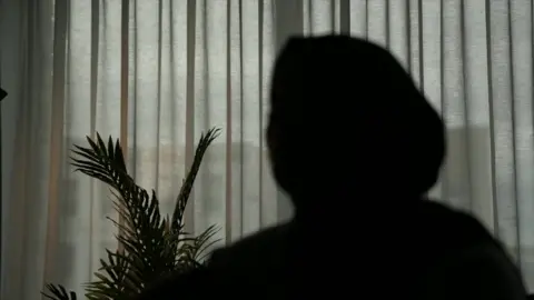 Outline of a woman against a window with curtains drawn. 