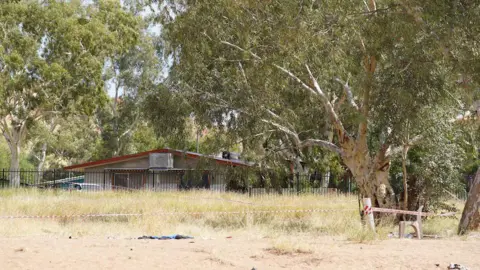 A photo of a dry river bank behind the Old Timers Camp, which can be seen in the background