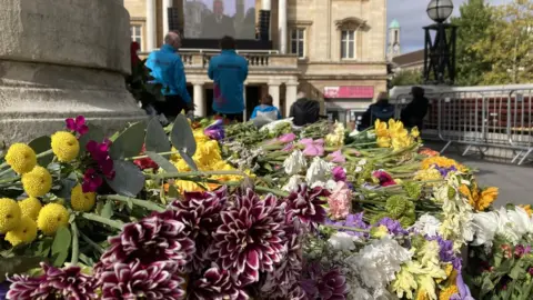 Flowers around statue with big screen in the distance